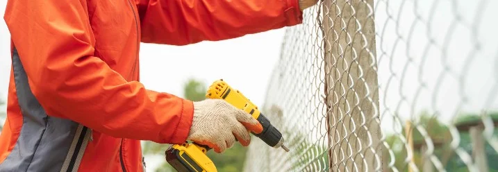 Person befestigt einen Maschendrahtzaun mit Akkuschrauber